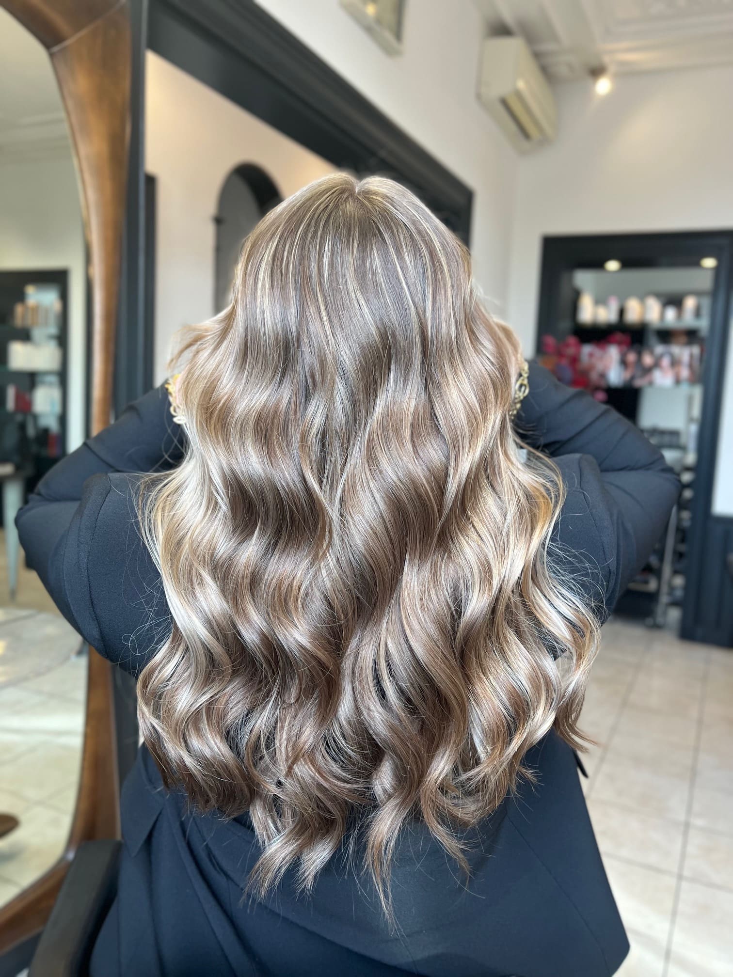 Lang blond dameskapsel in warme golven, gezien van achteren in de salon.